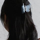 Person with long dark hair wearing a butterfly hair clip against a light background