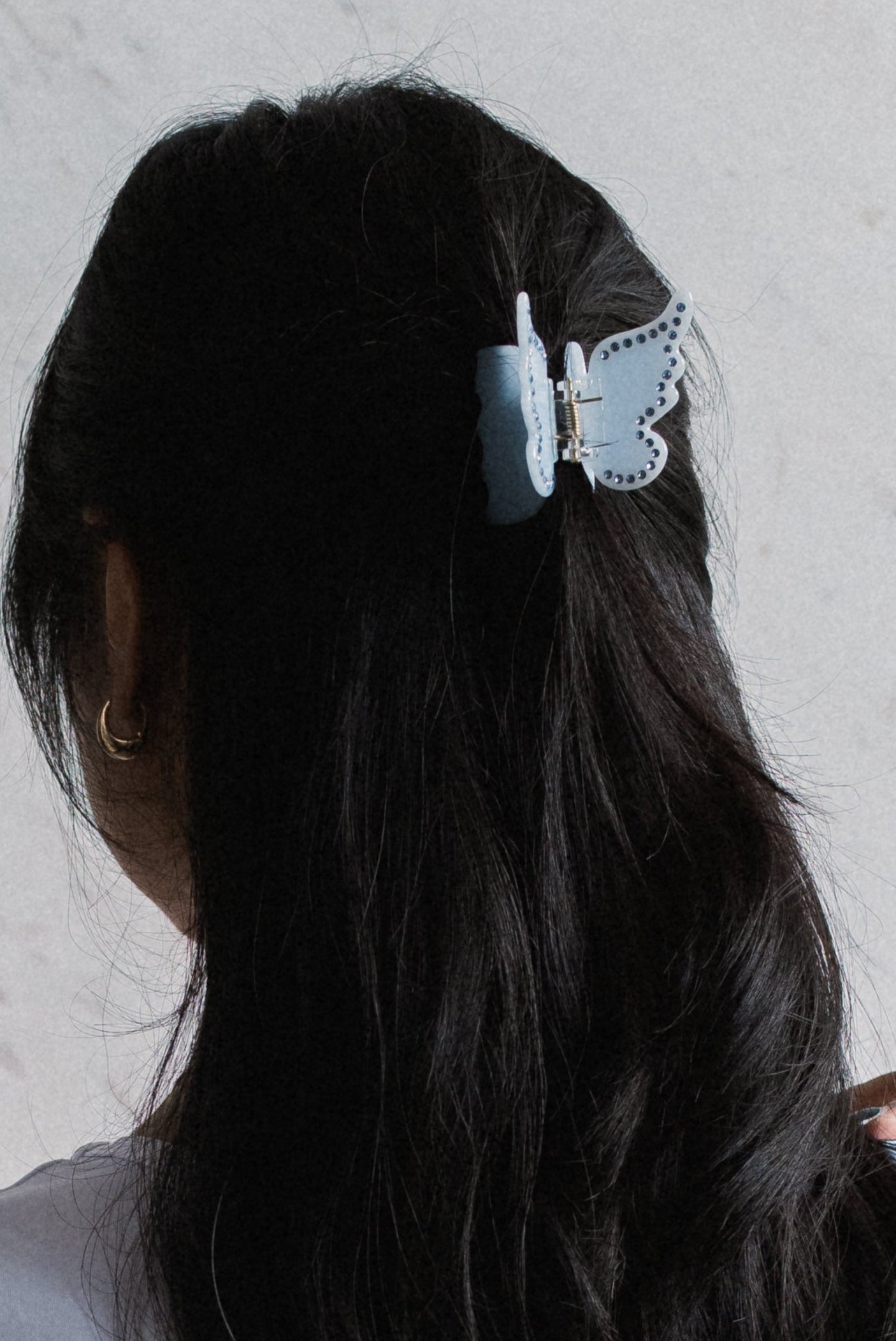 Person with long dark hair wearing a butterfly hair clip against a light background